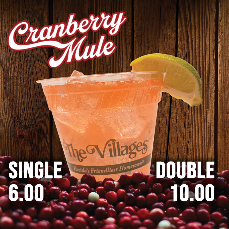 "Cranberry Mule." "Single $6." "Double $10." An orange drink, in a cup with The Villages logo and a lime wedge on the rim, sits in a pile of cranberries. Wood panels make up the background.